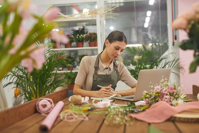 facebook ad account: image of a woman sitting at a desk in a flower shop, in front of a computer, managing the business