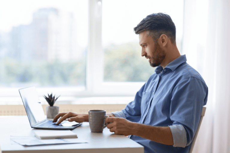 contato leads: imagem de um homem com camisa social azul digitando em um notebook e segurando uma caneca