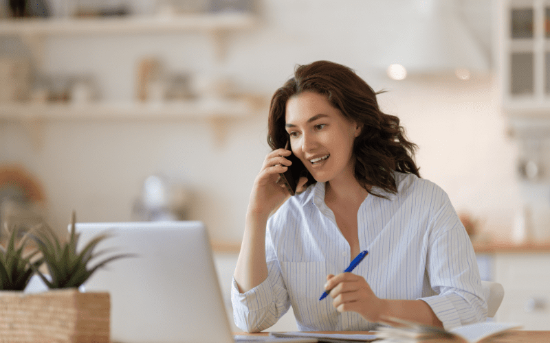 Tipos de campañas de anuncios de Google: mujer sentada delante de un ordenador, con camisa blanca, sosteniendo un bolígrafo y un teléfono móvil junto a la oreja.