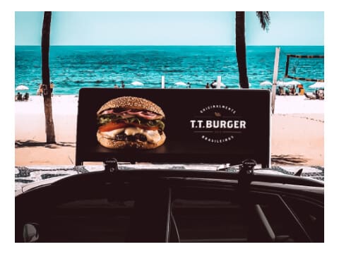 Topo do funil marketing: imagem de um anúncio de uma hamburgueria no visor em cima de um carro passando em frente a praia