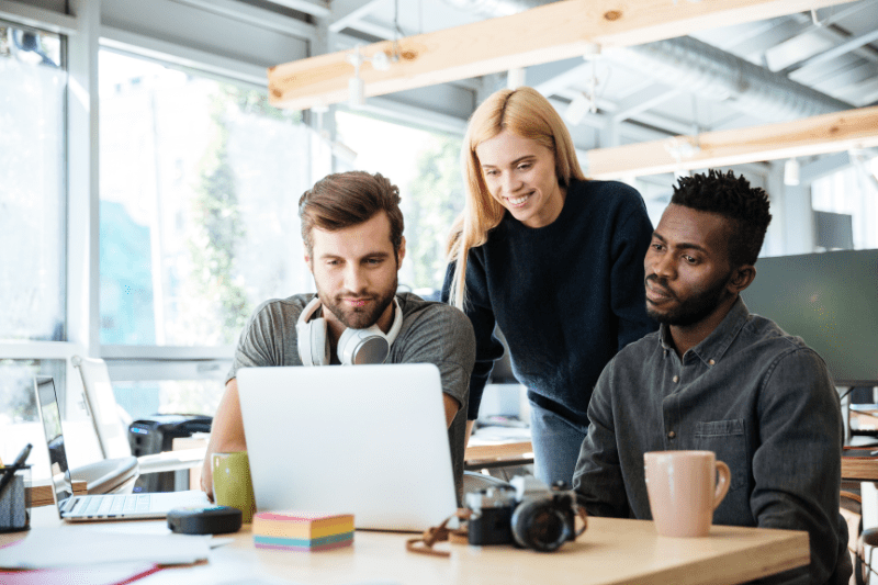 Beneficios de automatizar processos: imagem de três colegas felizes sentados no escritório olhando para um notebook