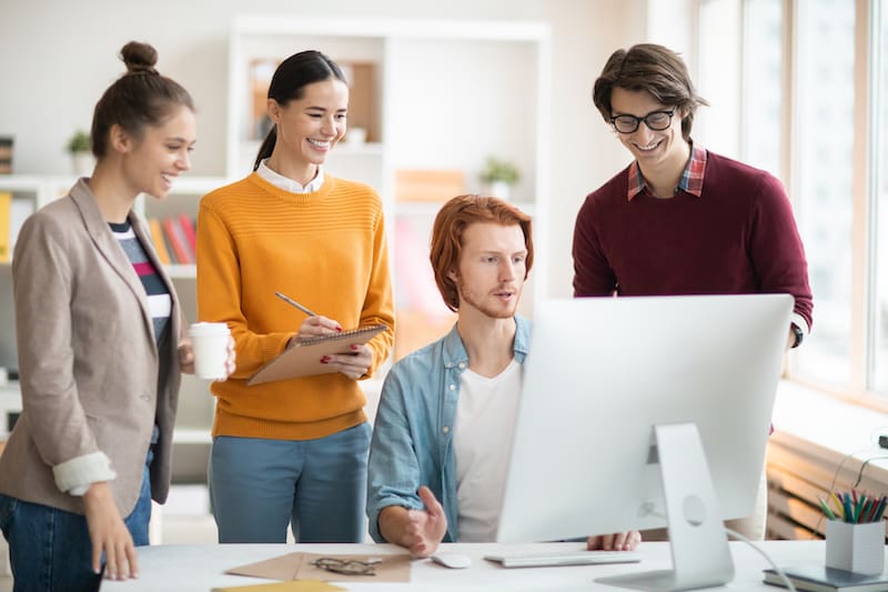 Automatización del marketing para agencias: imagen de cuatro personas en la oficina charlando y mirando la pantalla del ordenador
