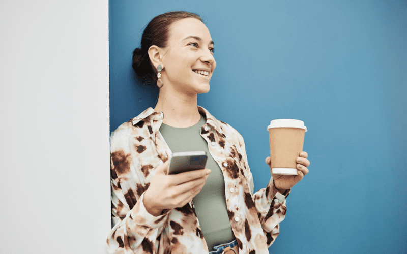 Squid: imagem de uma mulher branca jovem, sorrindo, segurando um café em uma mão e um celular na outra