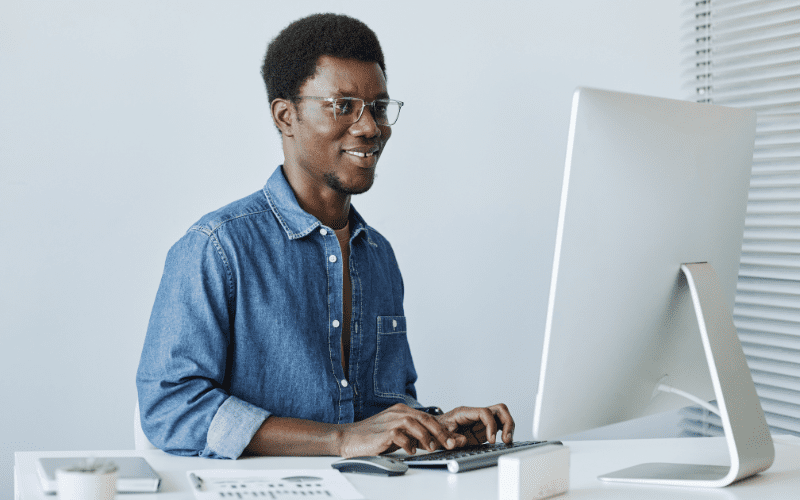 google performance max: image of a black man wearing glasses and walking socially in an office typing on a keyboard and looking at a computer screen