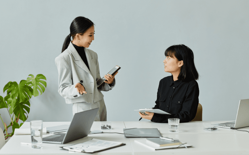 automatizacion de negocios: imagen de dos mujeres de negocios charlando en una mesa de reuniones con papeles y un cuaderno.