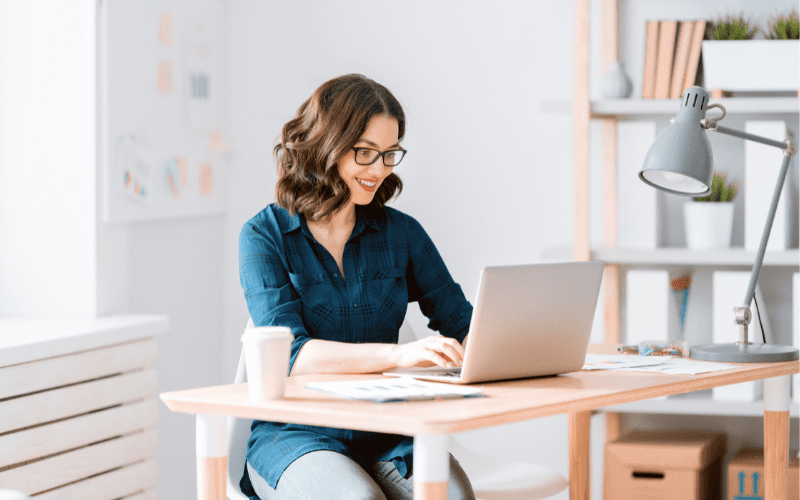 CAC e CPA: imagem de uma mulher usando óculos e camisa azul escuro digitando em um laptop