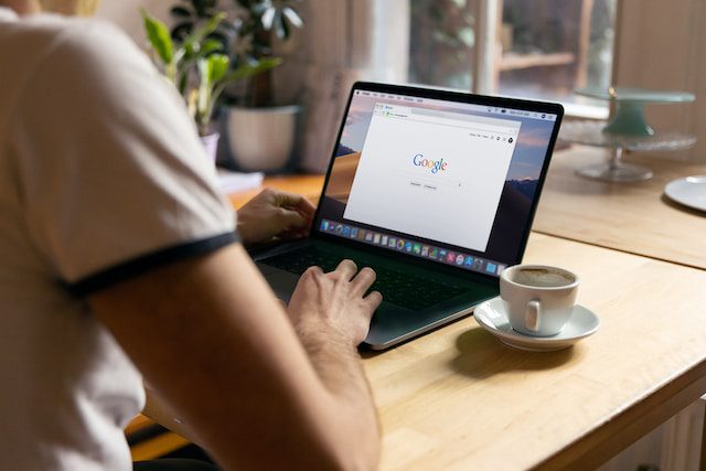 Tráfego pago: homem de costas, com blusa branca, mexendo no notebook com a tela do Google aberta.