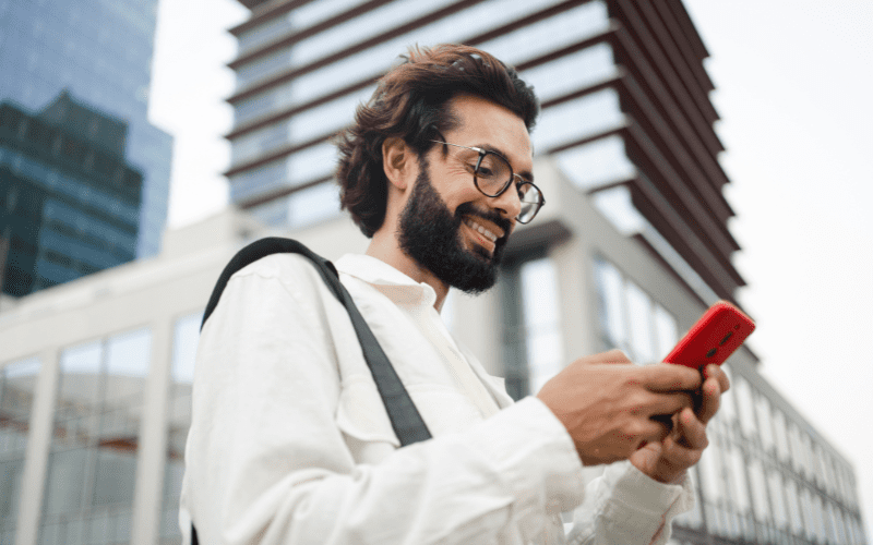 Instagram Ads: homem jovem com uma camisa branca, mexendo no celular na cidade e sorrindo