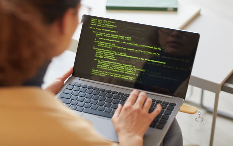 IA para Programação: imagem de uma mulher de costas, olhando para o código na tela do seu computador.