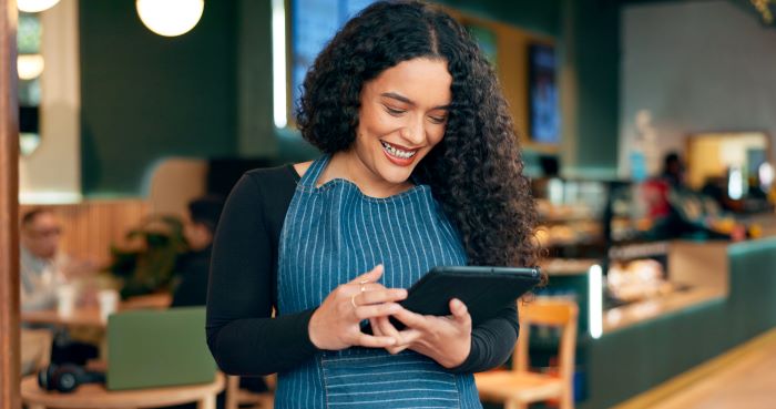 Exemplos de Inteligência Artificial: mulher negra, usando um avental e sorrindo para o seu Ipad.