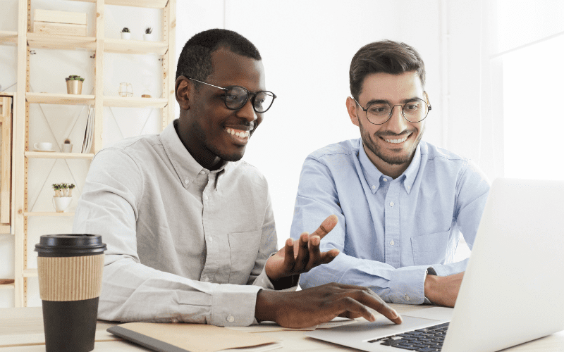 IA generativa: dos hombres con camisa de vestir sonríen y miran a un ordenador.