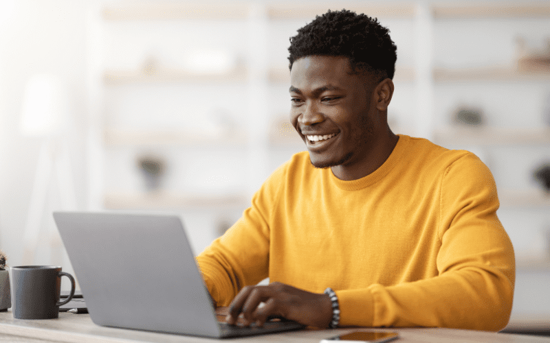 facebook ad library: image of a young black man, wearing a yellow blouse, typing on a laptop on a table