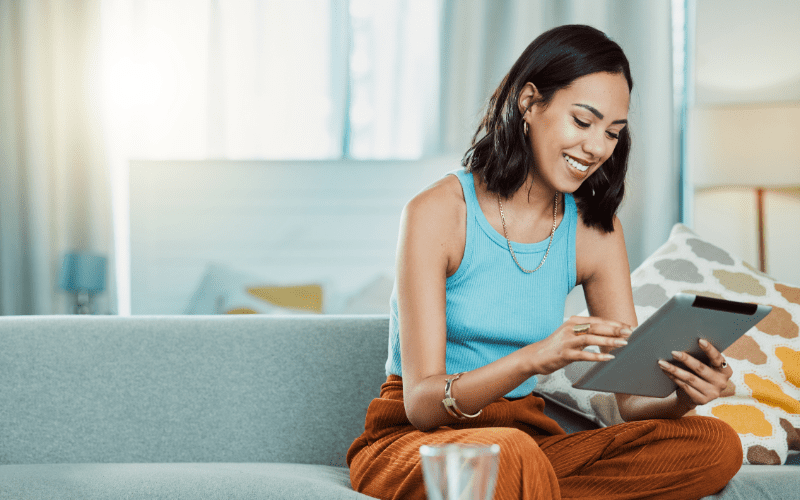 Captação de Leads em Mídia Paga: imagem de uma jovem do cabelo escuro, vestida com uma regata azul, olhando para seu IPad com uma expressão feliz.