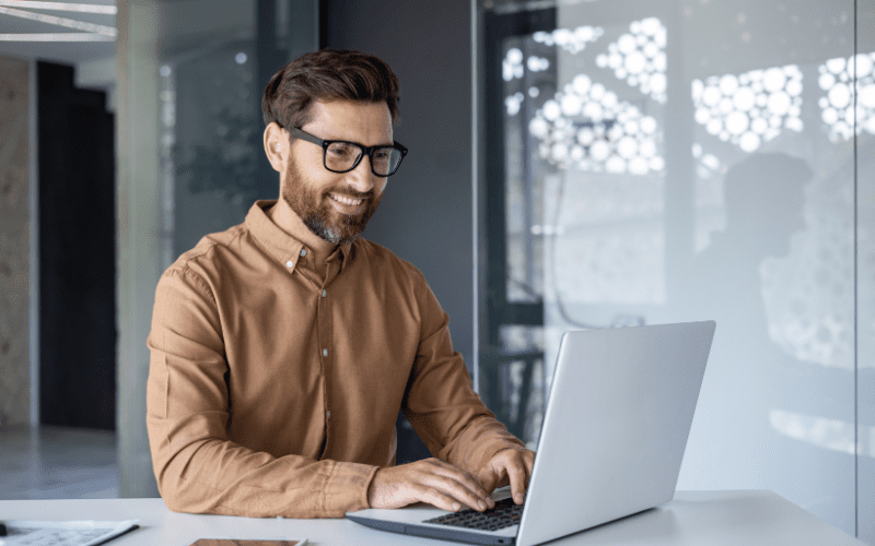 Ética e Inteligencia Artificial: una imagen de un hombre blanco con barba roja, vestido con ropa social y sonriendo a su ordenador.