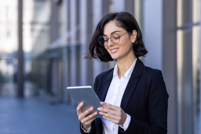 Proteção de Dados: imagem de uma jovem mulher vestida de social, sorrindo e olhando para o seu Ipad