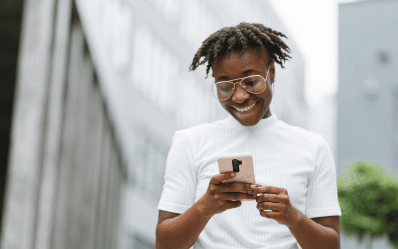 Artificial Intelligence and User Experience: young black woman in a white blouse looking at her smartphone
